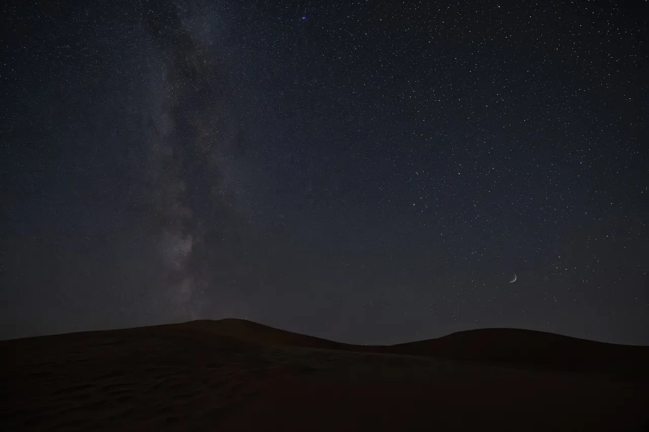 A star-filled sky above a dark dune silhouette.