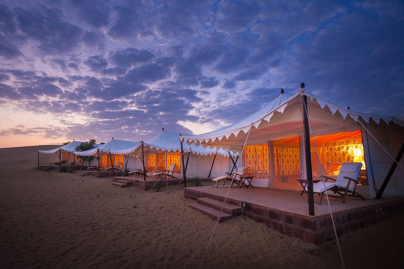 Illustrative tent interior with rugs, cushions, and lantern light.